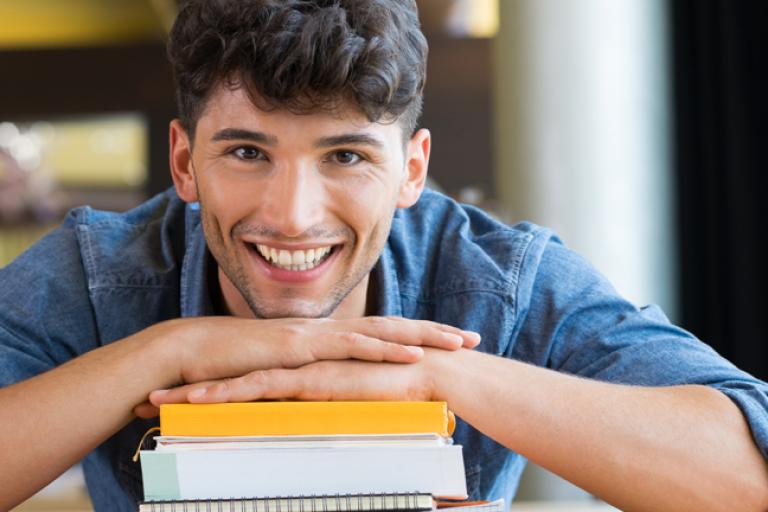 alpadia university pathway student smiling on top of books